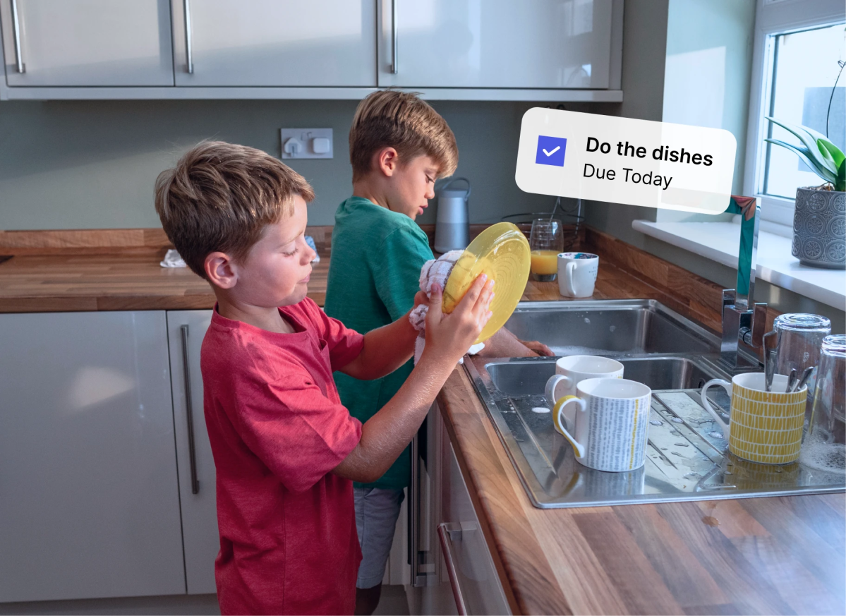 Two children wash dishes at a kitchen sink beside a task reminder bubble, showing families grow with Mydoh to learn money and finance.