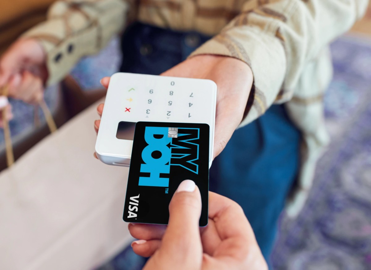 Hands tap a black Mydoh Visa card on a payment terminal, showing how it works to spend money and make contactless purchases.