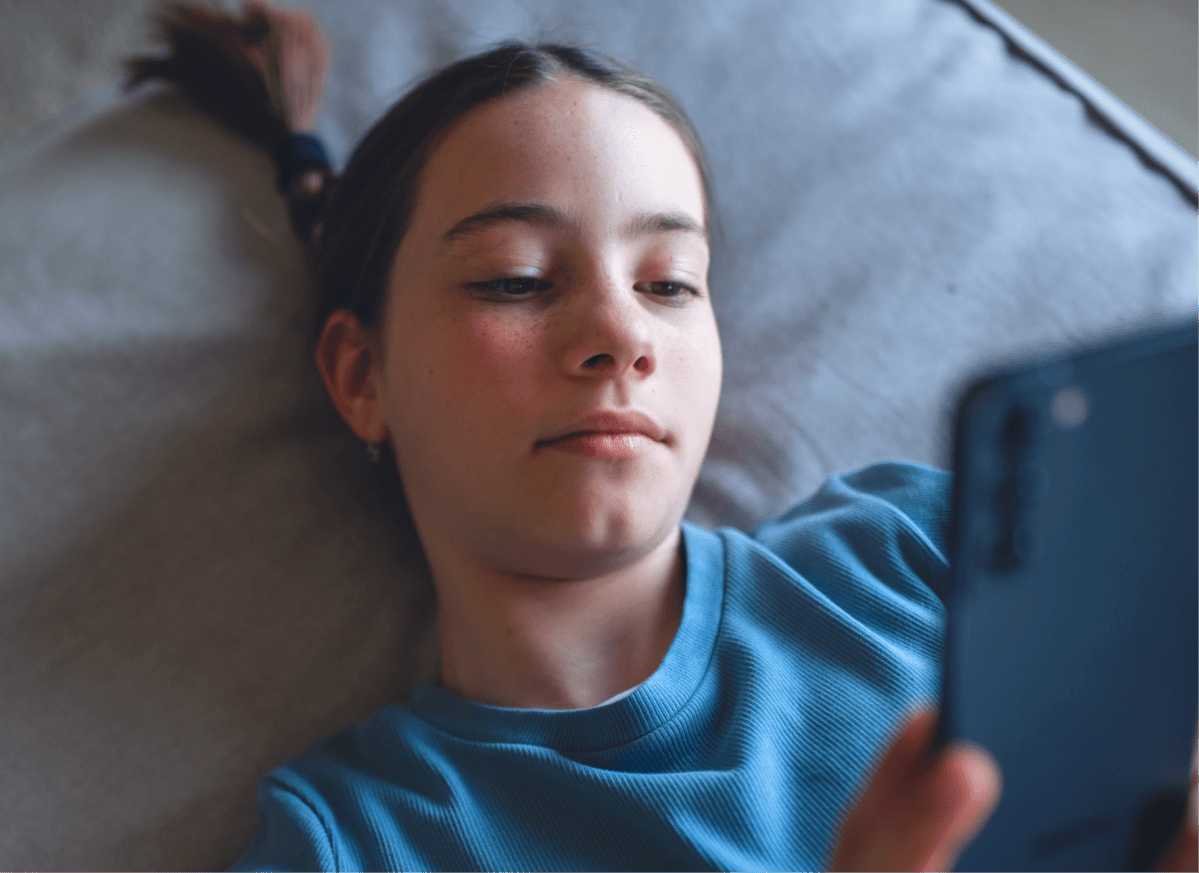 A young person lies back looking at a mobile phone, showing how it works to track money and savings with the Mydoh app