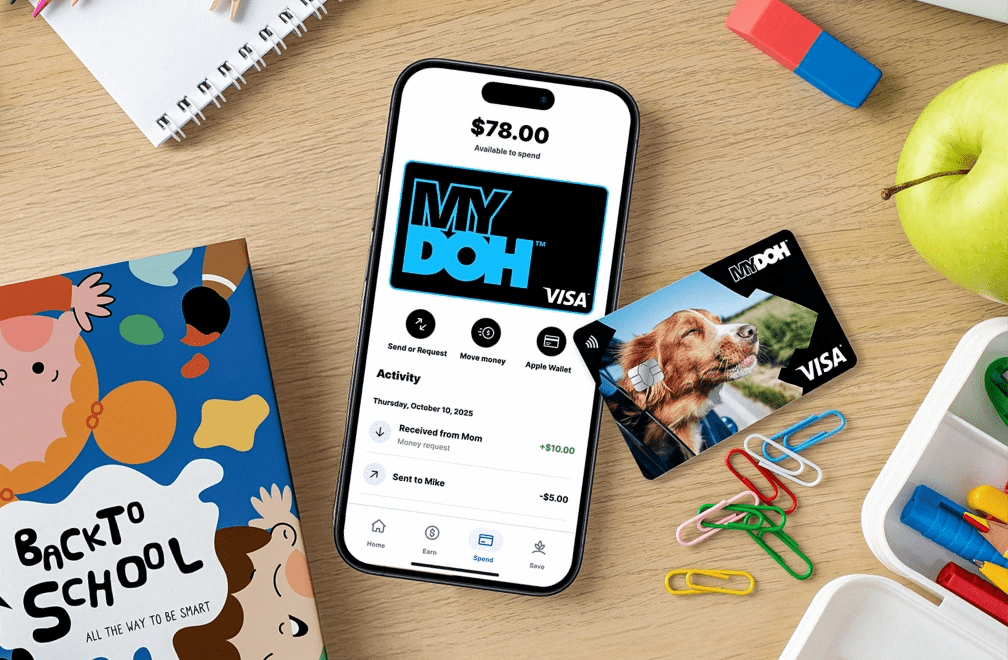 Flat lay mobile: app MyDoh affichant 78 $ disponibles, carte Visa et fournitures scolaires comme cahiers et pomme sur un bureau.