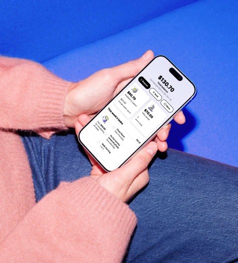 How it works: person in pink sweater holds a smartphone showing a money and task management app with balance, savings, and weekly tasks.