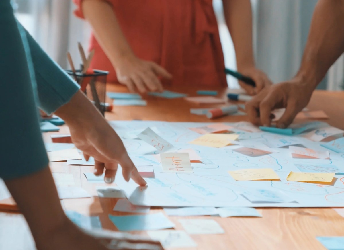 A team gathers around a table covered in colorful sticky notes and diagrams, collaborating on a planning session with markers and charts.